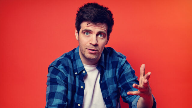 man with dark hair in front of a red background